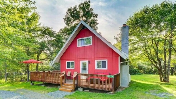 A red cabin with a wooden deck, a chimney, and a gravel driveway.