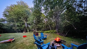 A backyard with a fire pit, blue Adirondack chairs, and a shuffleboard table.