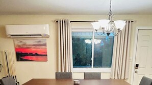 A dining room with a large wooden table, cushioned benches, a chandelier, and a large window with curtains.