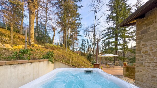 Ein Whirlpool in einem Garten mit Steinmauer, Holzterrasse und einer Terrasse mit Gartenmöbeln.