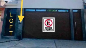 Ein modernes Gebäude mit einer Garage, deren Tür mit „LOFT“ beschriftet ist, und einem Verbotsschild für das Parken.