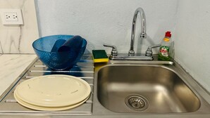 Ein Edelstahl-Spülbecken mit integriertem Wasserhahn, eine blaue Glasbowl, ein grüner Schwamm und eine Flasche Geschirrspülmittel.