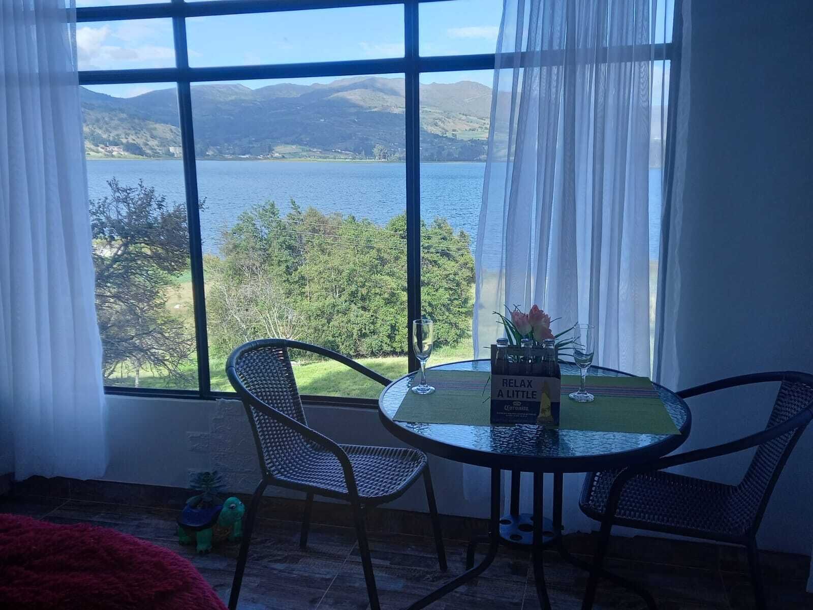 Huoneessa on suuri ikkuna, josta avautuu näkymä järvelle ja vuorille. Huoneessa on pyöreä lasipöytä, kaksi tuolia ja pullo Corona-olutta.