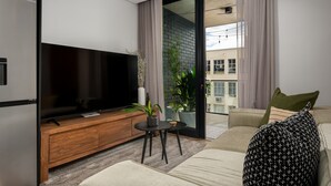 A modern living room with a flat-screen TV, wooden entertainment unit, a small round table, and a sofa. - Station House Luxury Living - Generator + Pool (Cape Town)