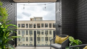 A balcony with a view of a building, featuring a grey chair with a yellow pillow and a potted plant. - Station House Luxury Living - Generator + Pool (Cape Town)