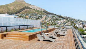 A rooftop pool area with lounge chairs and a view of a hill with a distinctive peak. - Station House Luxury Living - Generator + Pool (Cape Town)