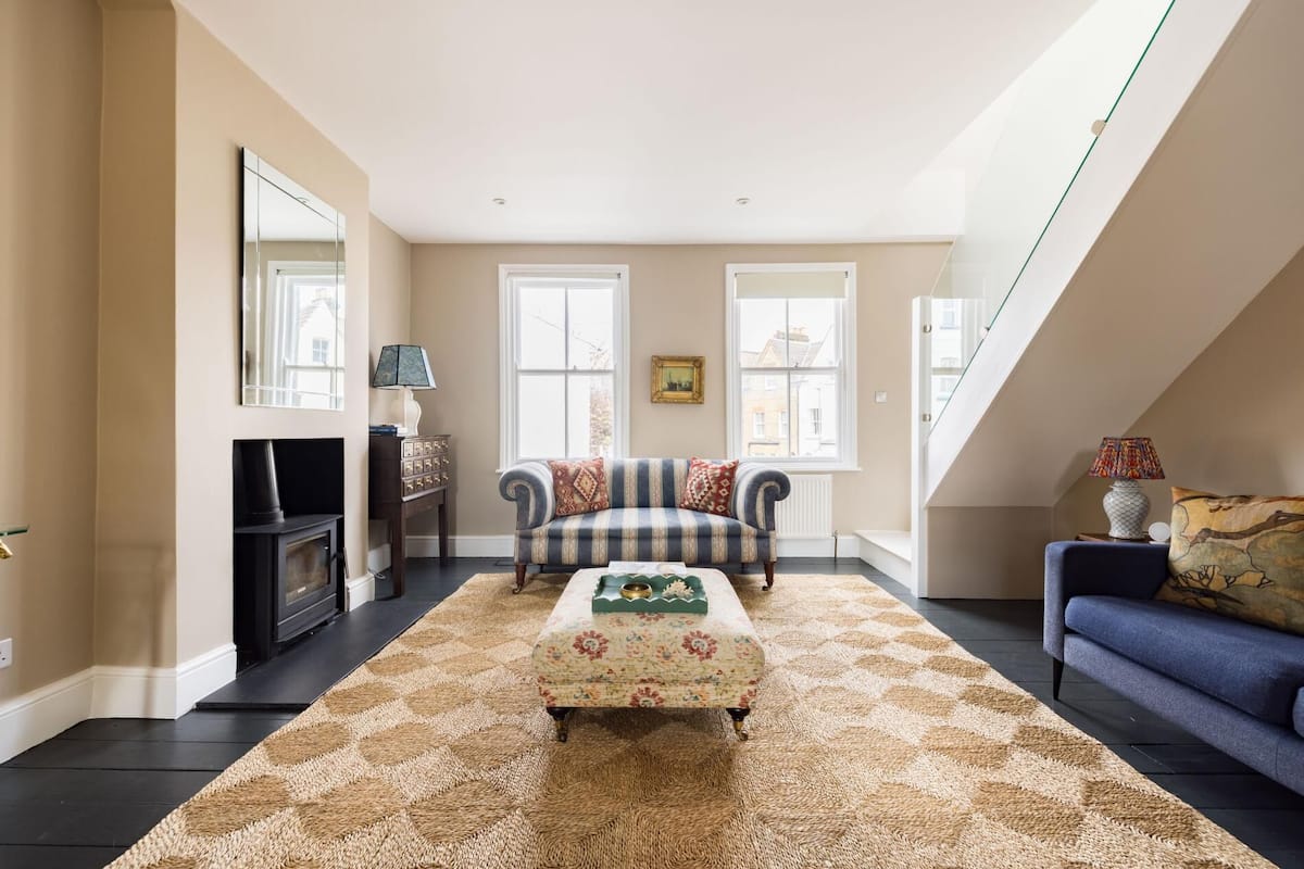A spacious living room with a large window, a fireplace, a sofa, and a patterned rug.
