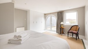 A hotel room with a large bed, a chair, a lamp, and a view of the outside. - The Thames Embrace 3 BR & Garden House (London)