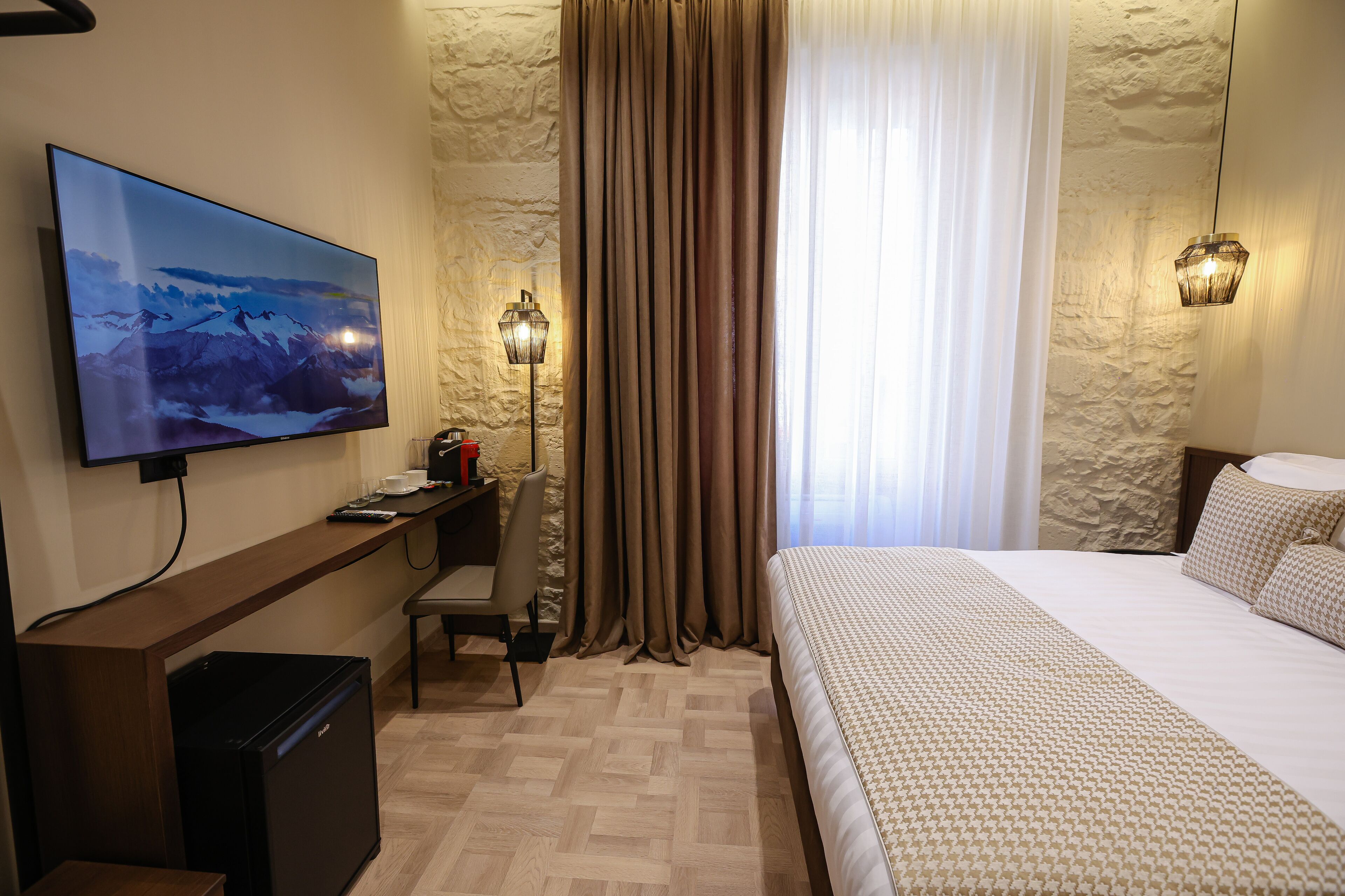 A hotel room with a bed, a desk, a chair, a television, and a small refrigerator.