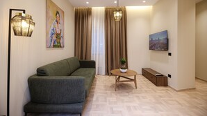 Un salon moderne avec un canapé, une petite table ronde agrémentée d’une plante, un tableau et un téléviseur fixé au mur.