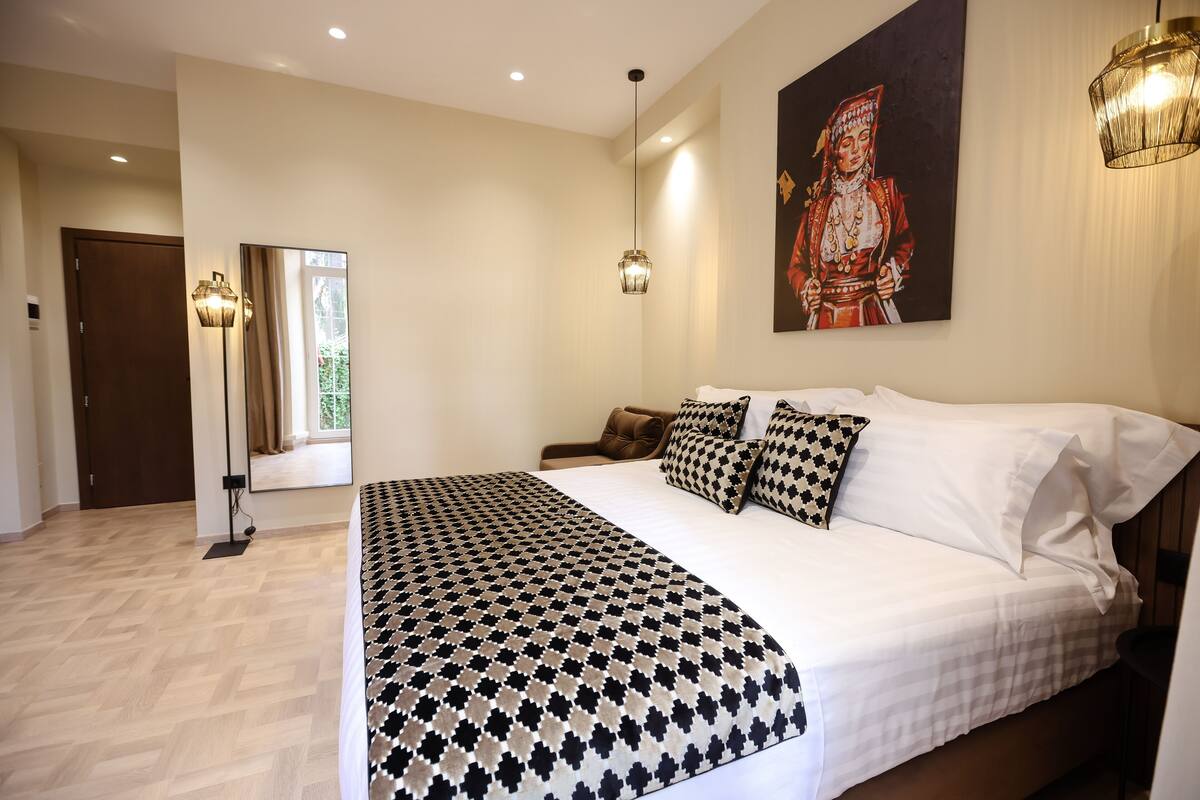 A bedroom with a large bed, a mirror, a painting, and a floor lamp.