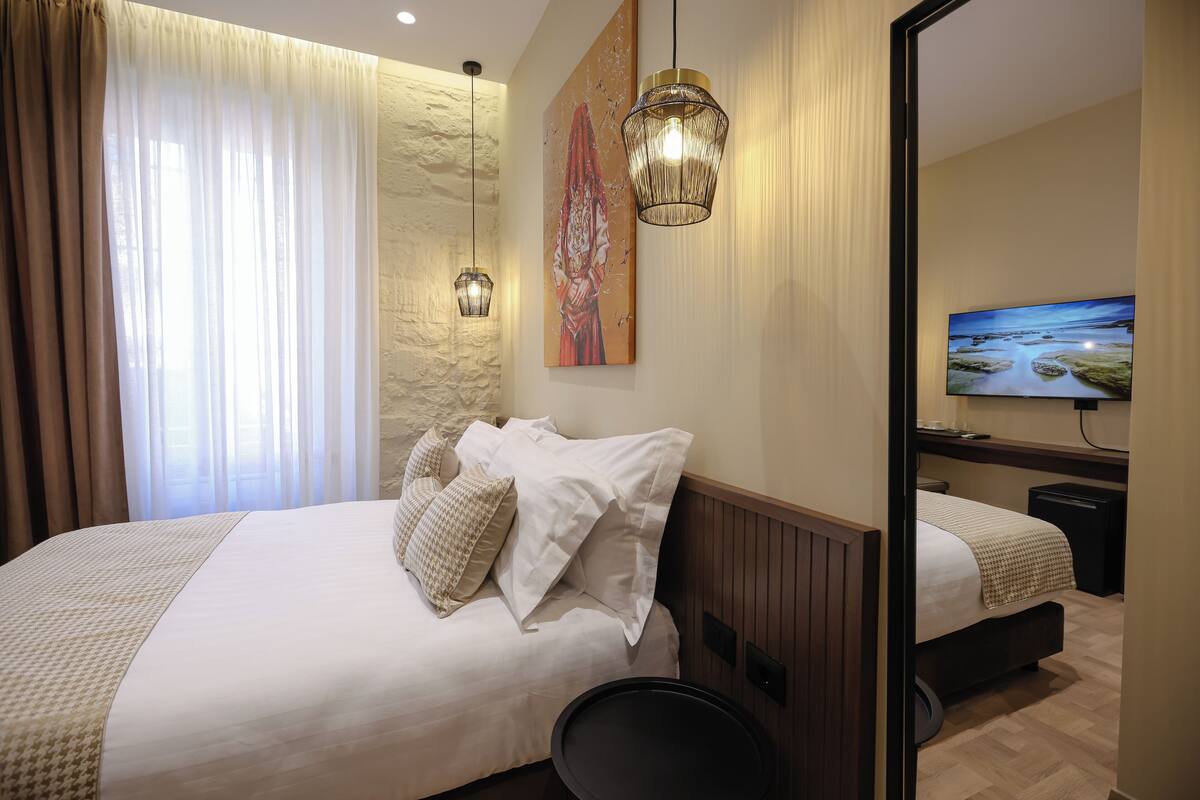 A hotel room with a large bed, a bedside table, a mirror, and a television.
