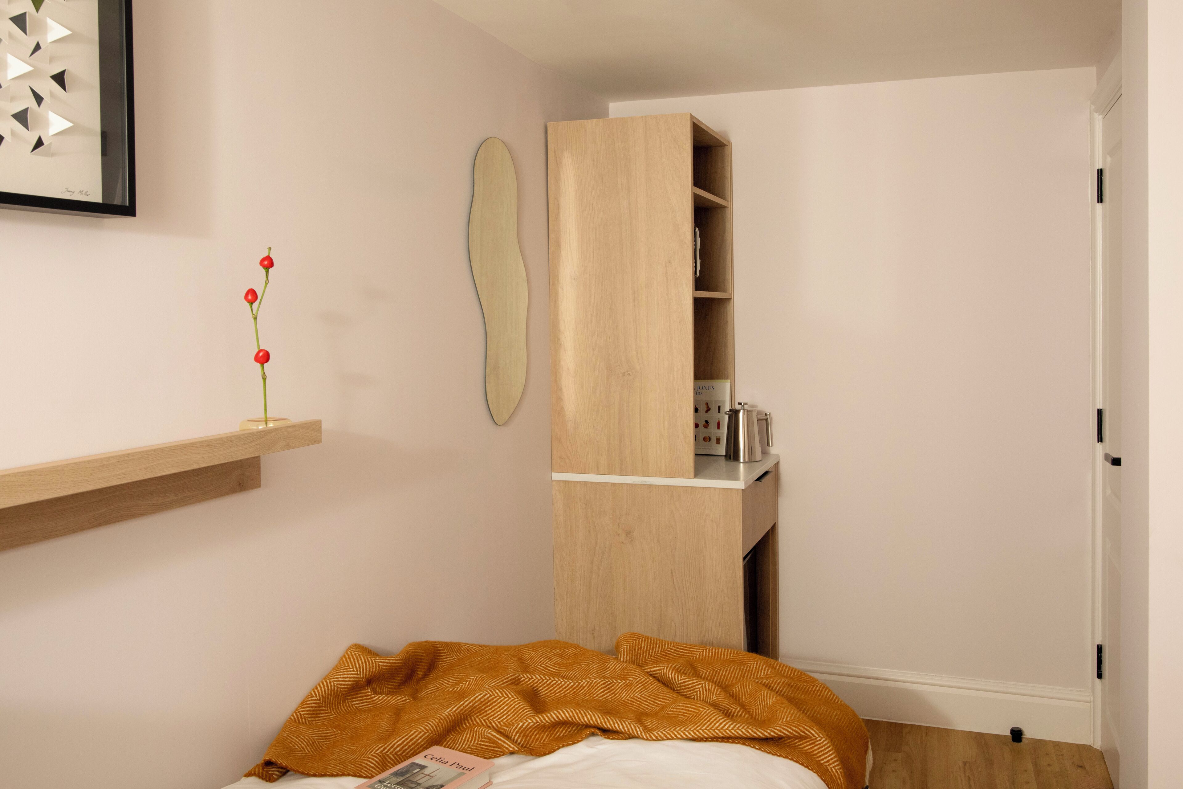 Een slaapkamer met een bed, een houten garderobe, een plank met een vaas en een lijst met een foto aan de muur.