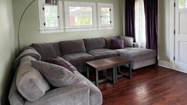 A living room with a sectional sofa, a coffee table, and a ceiling fan. There are three windows with white frames and curtains. - Spacious & Inviting Bungalow near Downtown
 (Phoenix)