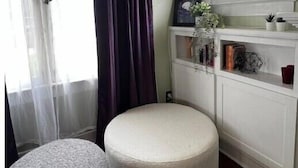 A room with a large window, a dark curtain, a white bench, and a shelf with books and decorative items. - Spacious & Inviting Bungalow near Downtown
 (Phoenix)