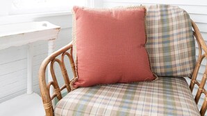 Una habitación con paredes de madera blanca, una silla de mimbre con cojines a cuadros y un cuadro en la pared.