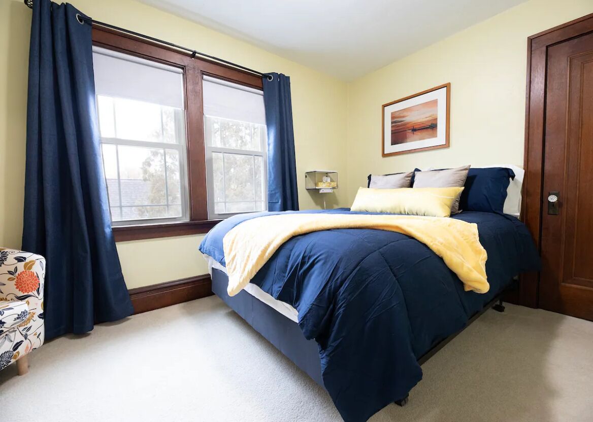 A bedroom with a bed, a window with curtains, a bedside table, and a door.