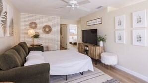 Un dormitorio con cama, televisor, ventilador de techo y pared de ladrillo.
