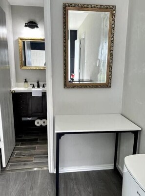 A bathroom with a white vanity, a mirror with a decorative frame, a toilet, and a shower area.