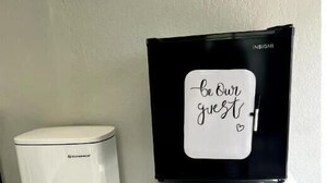 A compact kitchen setup with a white trash can, a microwave, and a black refrigerator with a sign that reads "be our guest." - Exclusive Loft (San Antonio)