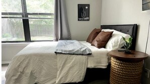 A bedroom with a bed, a bedside table with a plant, and a window with blinds. - Exclusive Loft (San Antonio)