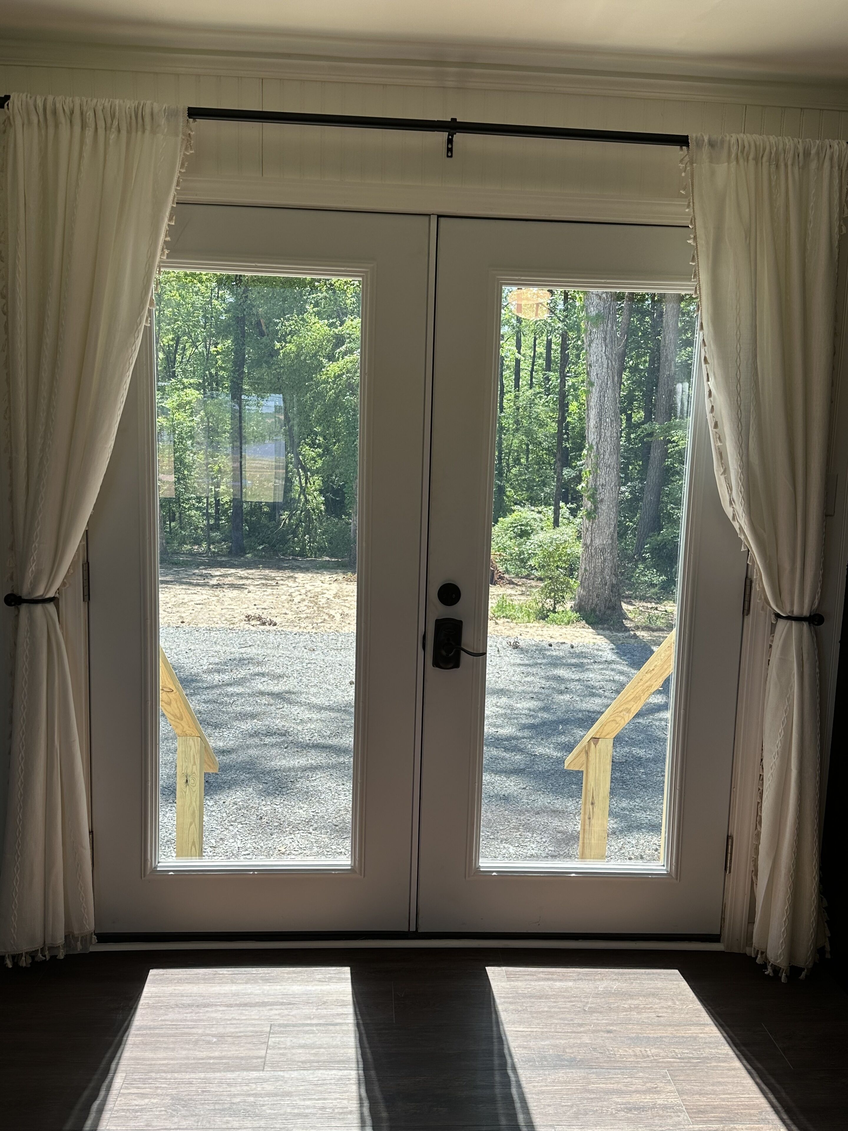 A double door with a view of a forested area and a wooden deck outside.