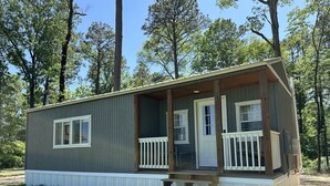 A small, single-story cabin with a porch, white railings, and a set of stairs leading to the entrance. - D'Arbonne Nest Rentals: The Gator's Nest (Union Parish)