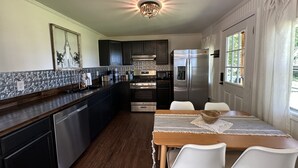 A kitchen with dark cabinets, a stainless steel refrigerator, and a dining area with a table and chairs. - D'Arbonne Nest Rentals: The Gator's Nest (Union Parish)