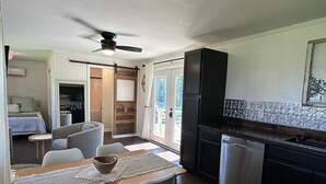 A modern kitchen with dark cabinetry, a stainless steel refrigerator, and a dining area with a wooden table and chairs. - D'Arbonne Nest Rentals: The Gator's Nest (Union Parish)