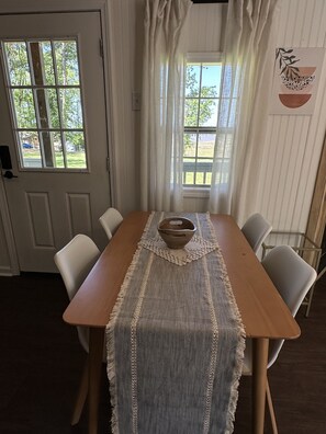 A dining area with a wooden table, white chairs, a woven table runner, and a bowl.