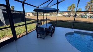 Eine überdachte Terrasse mit Pool, Sitzgelegenheiten im Freien und Blick auf einen Park.