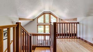 A room with a sloped ceiling, wooden flooring, a wooden railing, and a large window. - Charming Italian Villa Retreat • 10 Min to UO & Autzen (Eugene)