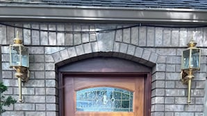A wooden front door with a glass panel, flanked by stone walls and two wall-mounted lanterns. - Charming Italian Villa Retreat • 10 Min to UO & Autzen (Eugene)