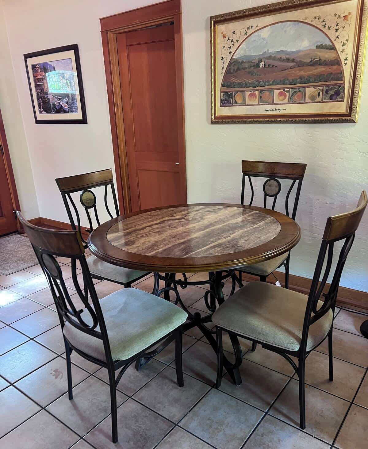 A dining area with a round table and four chairs, a framed picture on the wall, and a wooden door.