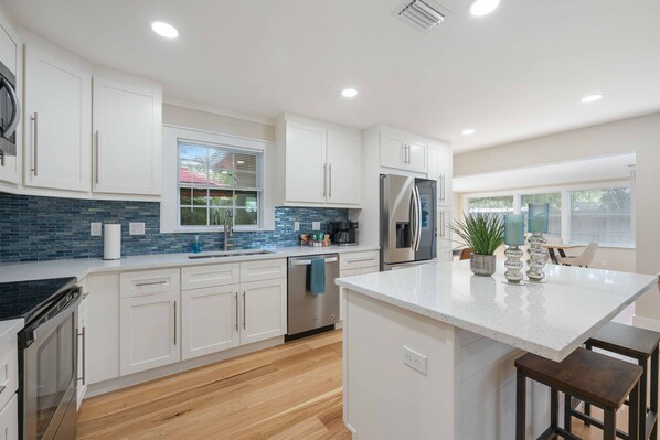 A modern kitchen with white cabinets, a stainless steel refrigerator, and a large island with bar stools.
