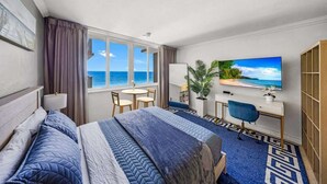 Habitación de hotel con cama, escritorio, silla, televisor y vista al océano.