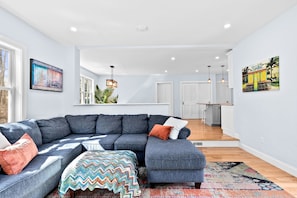 A modern living room with a sectional sofa, a colorful rug, and artwork on the walls. - Spacious new home 6-minute drive to beaches and historic Scituate Harbor! (Scituate)