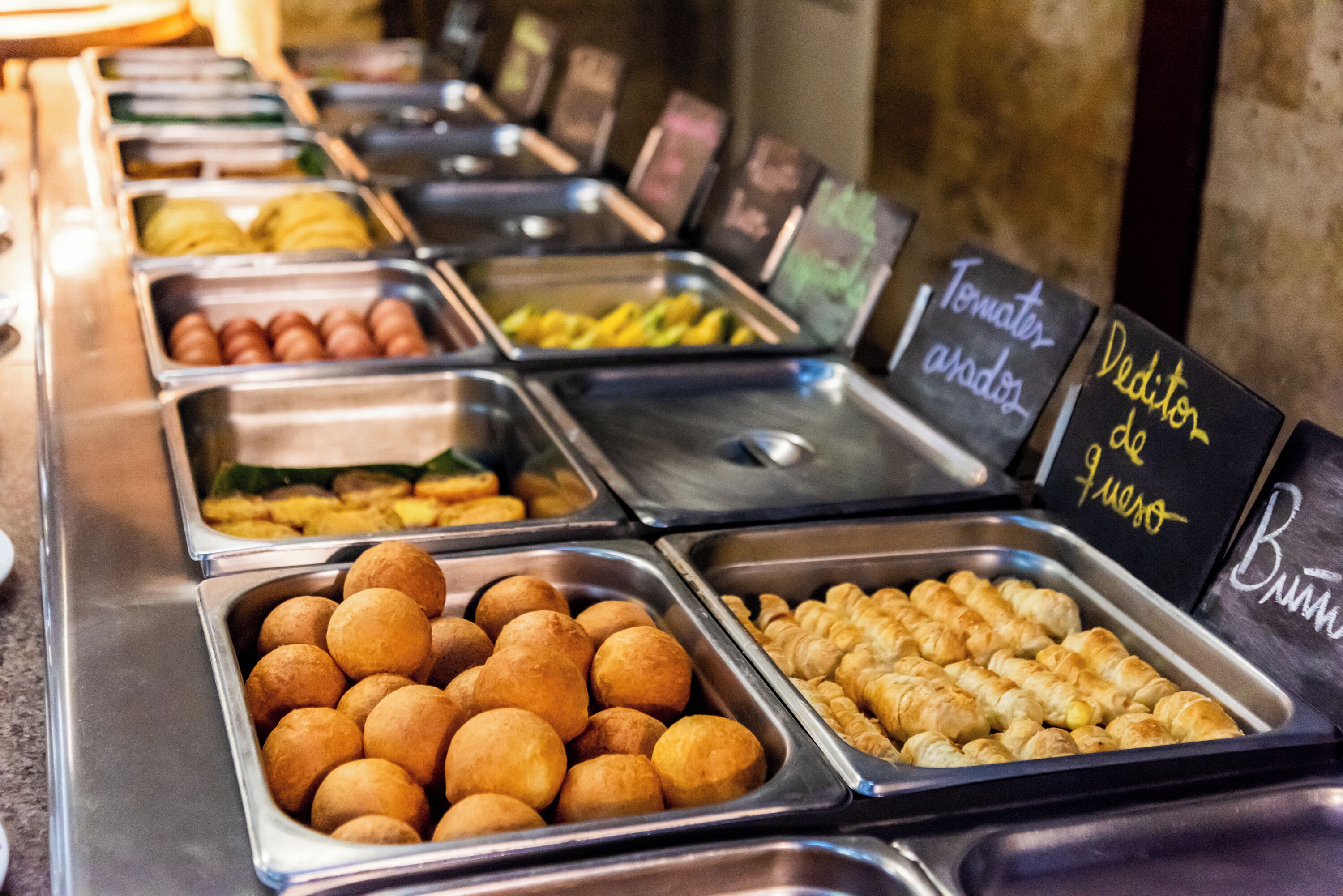 A buffet with various food items in metal containers, including what appears to be croissants and other pastries.