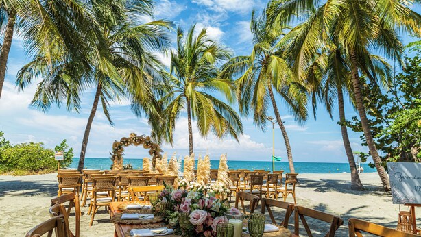 A beachside dining setup with tables set for two, surrounded by palm trees and ocean views. - Hotel Irotama XXI (Santa Marta)