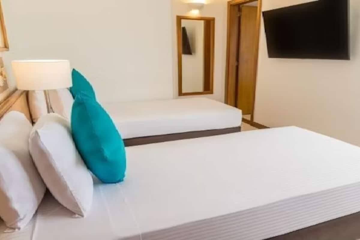A hotel room with two beds, a TV, a mirror, and a lamp.