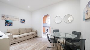 Ein modernes Wohnzimmer mit einem beige-farbenen Sofa, einem Glastisch mit Stühlen und einer Waschmaschine im Hintergrund.