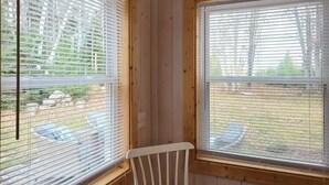 Una habitación con dos ventanas, cada una con persianas blancas, marcos de madera y vista a un espacio exterior con una mesa y sillas.