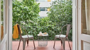 Ein Balkon mit zwei Stühlen und einem kleinen runden Tisch, mit Blick auf ein Gebäude und Grünflächen.