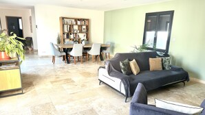 A living room with a sofa, a dining table with chairs, a bookshelf, and a potted plant.
