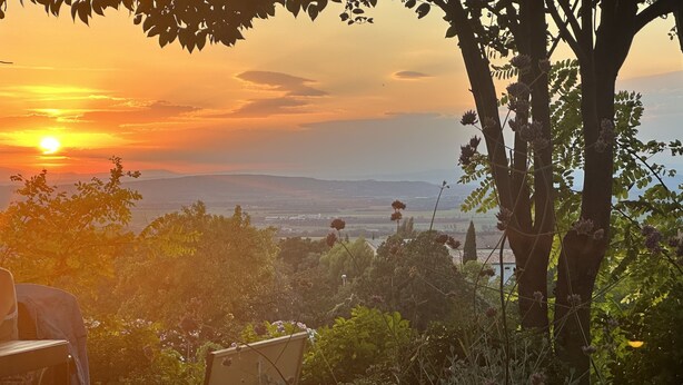 A garden with a table and chair, a view of the sunset, and a tree with flowers.