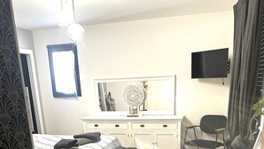 A bedroom with a bed, a bench, a desk, a chair, a TV, and a window.