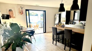 A modern kitchen with a dining area, featuring a large window, a dining table, chairs, and a potted plant.