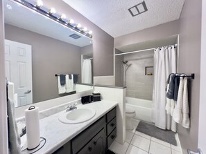 Enjoy a refreshing shower in the bathroom, featuring a glass-enclosed tub with a handheld showerhead and a white curtain.