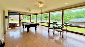 Une pièce spacieuse équipée d’une table de billard, d’un ventilateur de plafond et de grandes fenêtres donnant sur l’extérieur.