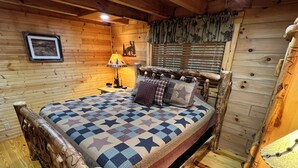 Een slaapkamer in een houten hutje, met een bed, een nachtkastje, een lamp en een raam met jaloezieën.